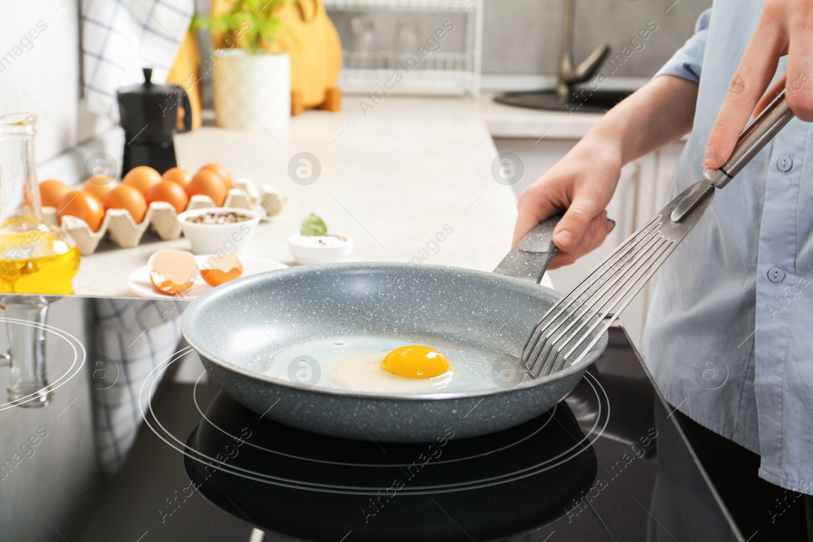 Photo of Woman with slotted turner cooking egg in frying pan on cooktop indoors, closeup