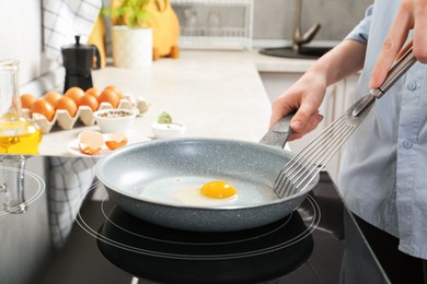 Photo of Woman with slotted turner cooking egg in frying pan on cooktop indoors, closeup