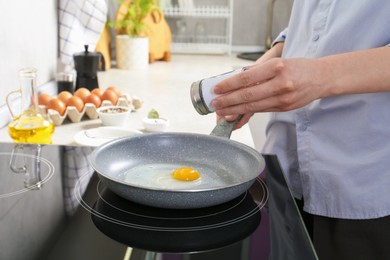 Photo of Woman adding salt into frying pan while cooking eggs on cooktop in kitchen, closeup