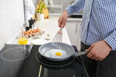 Photo of Man cooking egg in frying pan on cooktop indoors, closeup