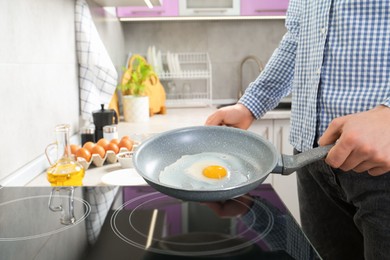 Photo of Man cooking egg in frying pan on cooktop indoors, closeup