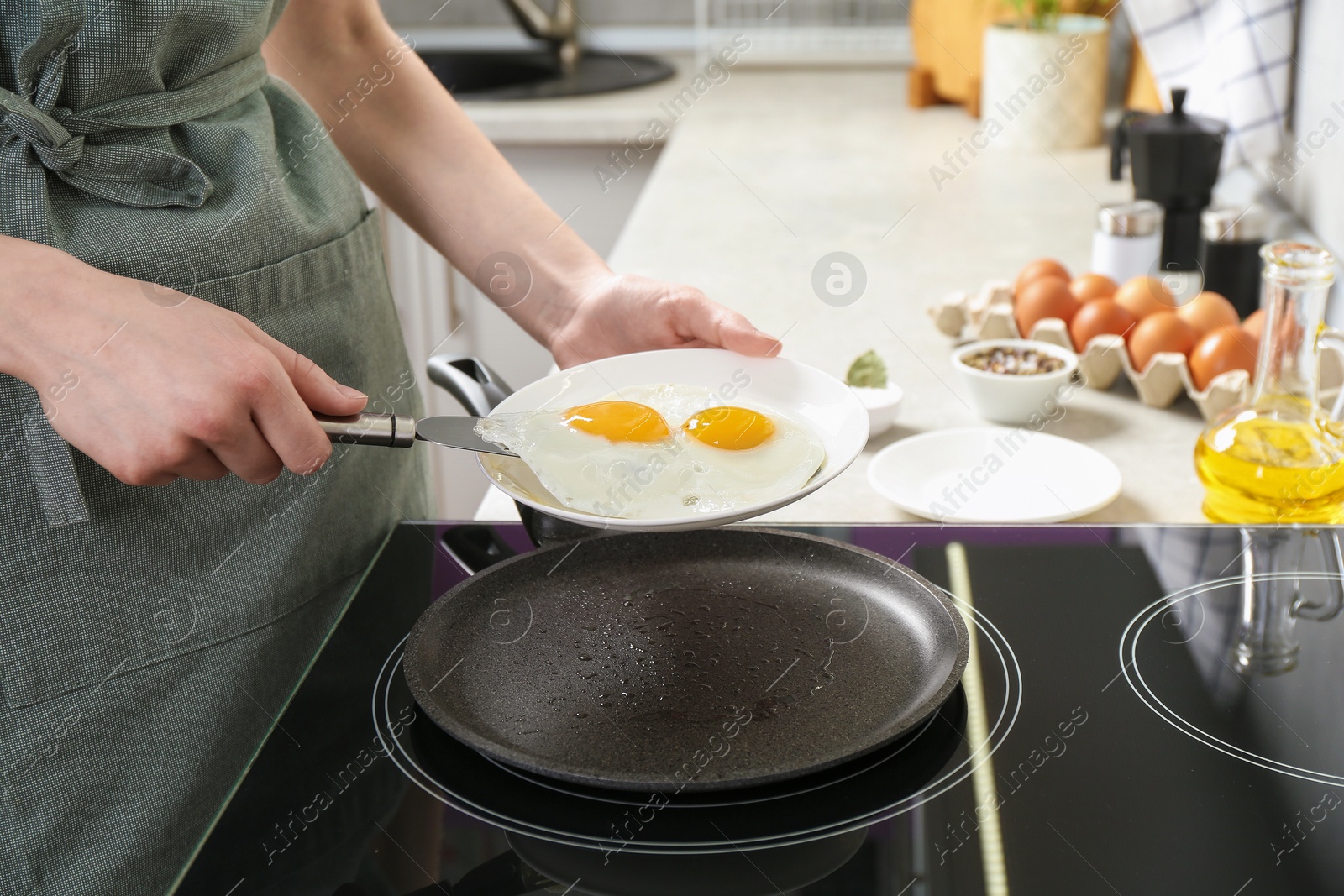 Photo of Woman putting tasty fried eggs onto plate in kitchen, closeup