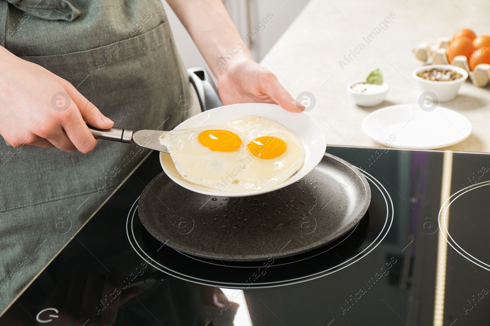 Photo of Woman putting tasty fried eggs onto plate in kitchen, closeup