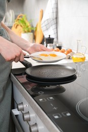 Photo of Woman putting tasty fried eggs onto plate in kitchen, closeup