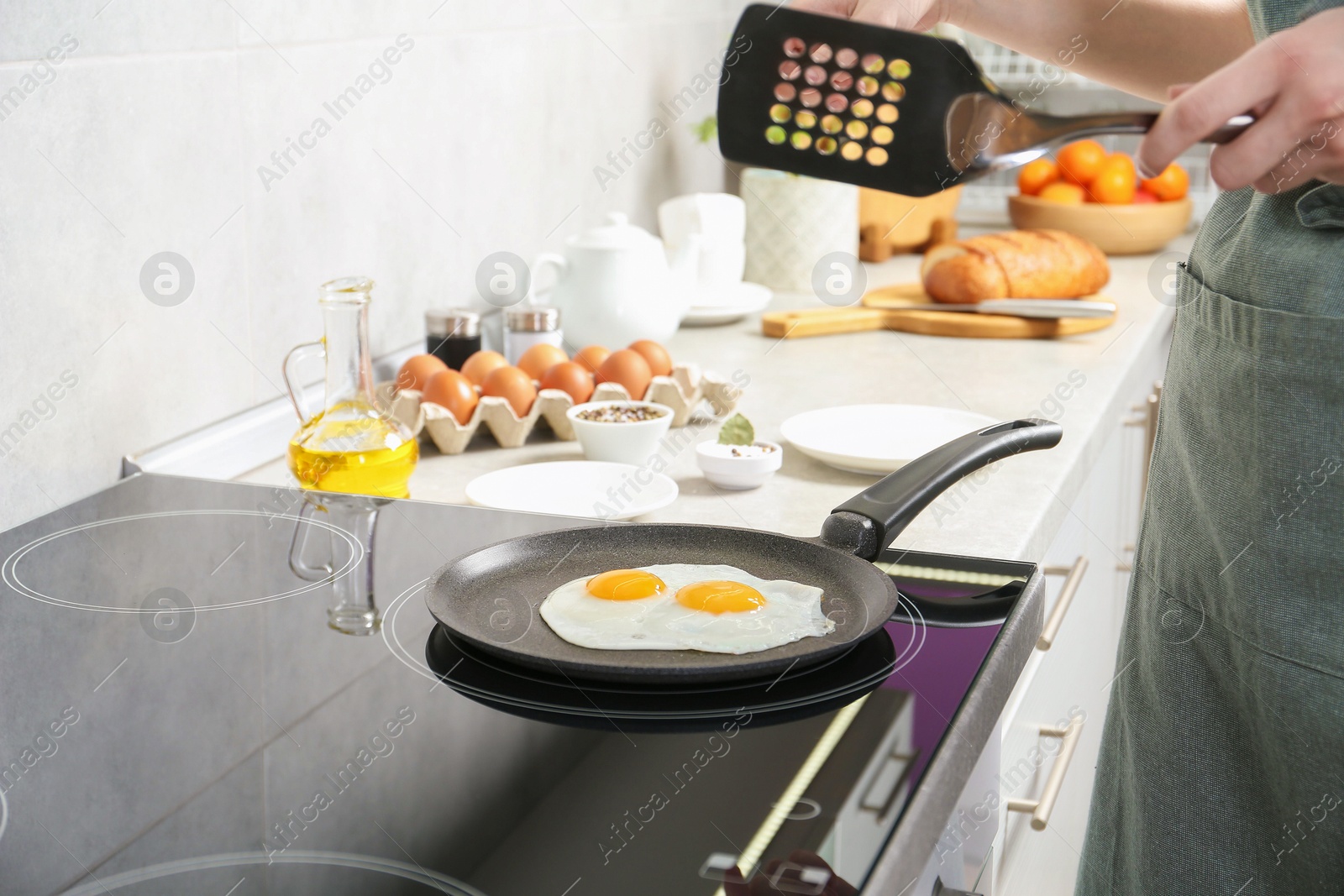 Photo of Woman with slotted turner cooking eggs in frying pan on cooktop indoors, closeup