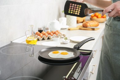 Photo of Woman with slotted turner cooking eggs in frying pan on cooktop indoors, closeup