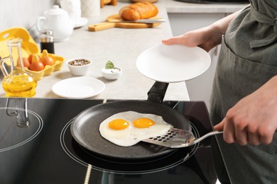 Photo of Woman taking fried eggs from frying pan in kitchen, closeup