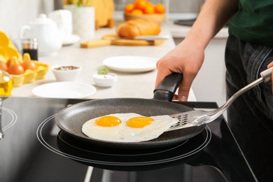 Photo of Man taking fried eggs from frying pan in kitchen, closeup