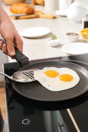 Photo of Man taking fried eggs from frying pan in kitchen, closeup