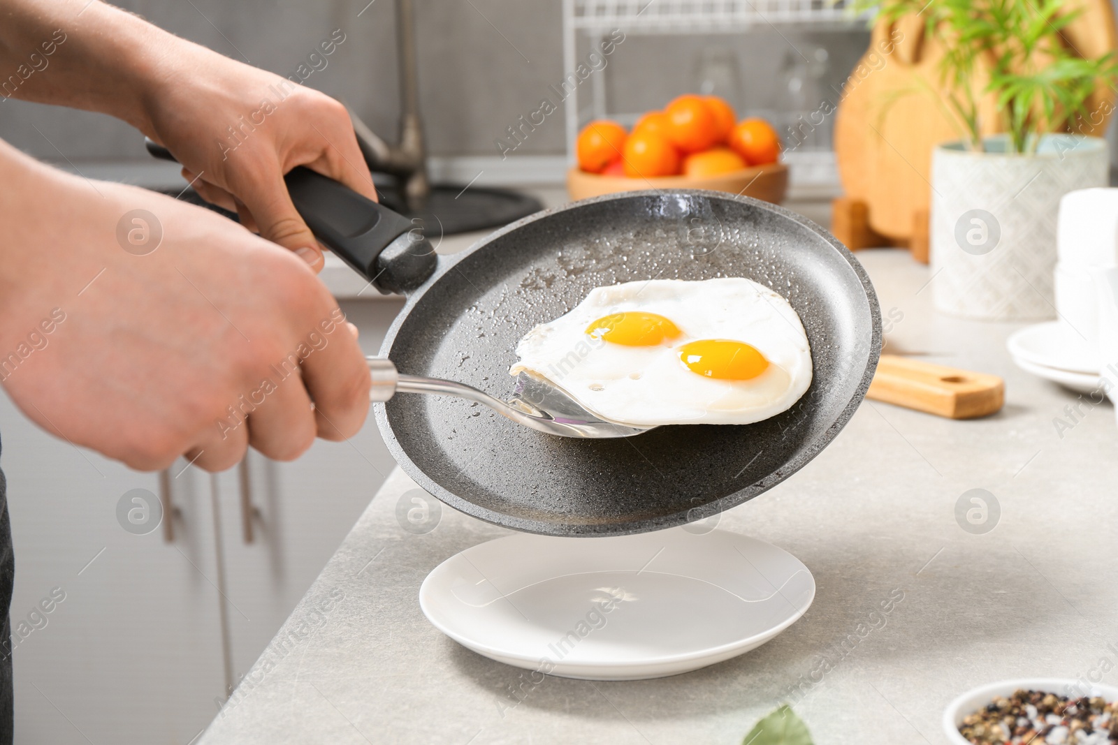 Photo of Man putting tasty fried eggs onto plate from frying pan in kitchen, closeup