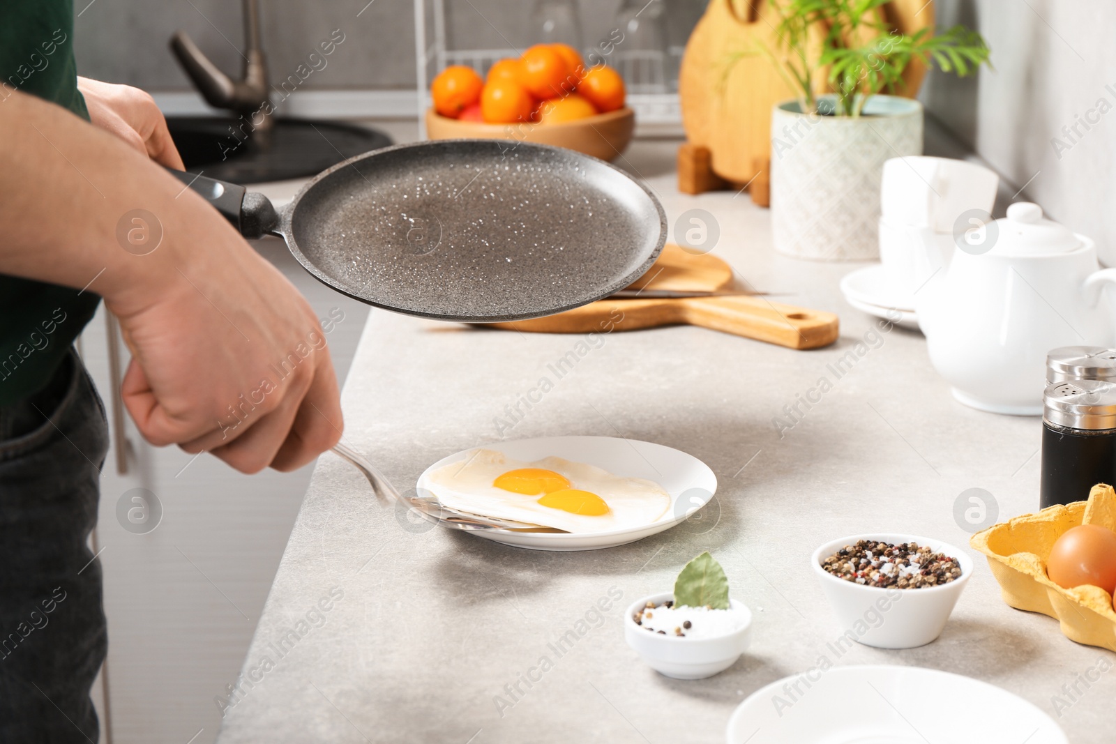 Photo of Man with frying pan putting tasty fried eggs onto plate in kitchen, closeup