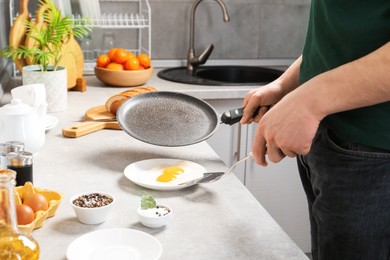 Photo of Man with frying pan putting tasty fried eggs onto plate in kitchen, closeup