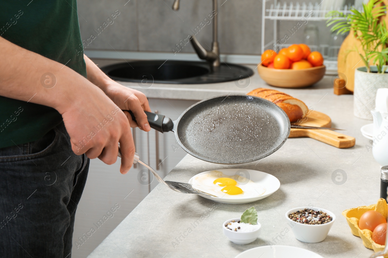 Photo of Man with frying pan putting tasty fried eggs onto plate in kitchen, closeup