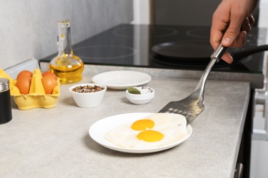 Photo of Man with frying pan putting tasty fried eggs onto plate in kitchen, closeup