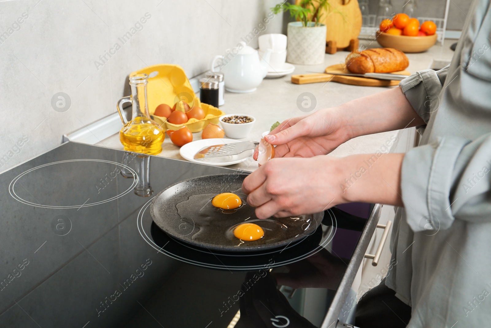 Photo of Woman breaking egg into frying pan in kitchen, closeup