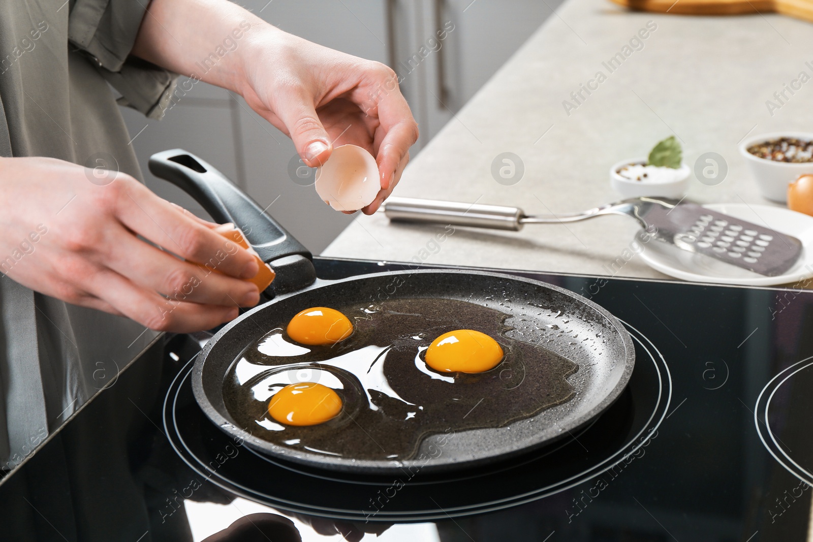 Photo of Woman breaking egg into frying pan in kitchen, closeup