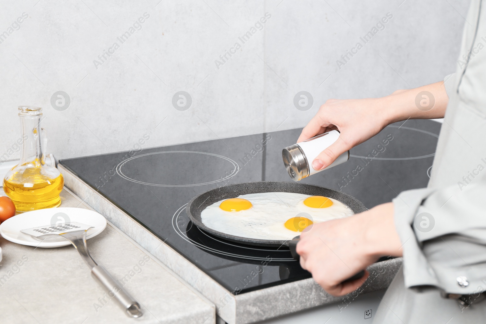 Photo of Woman adding salt into frying pan while cooking eggs on cooktop in kitchen, closeup