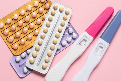 Photo of Blisters of oral contraceptive pills and pregnancy tests on pink background, flat lay