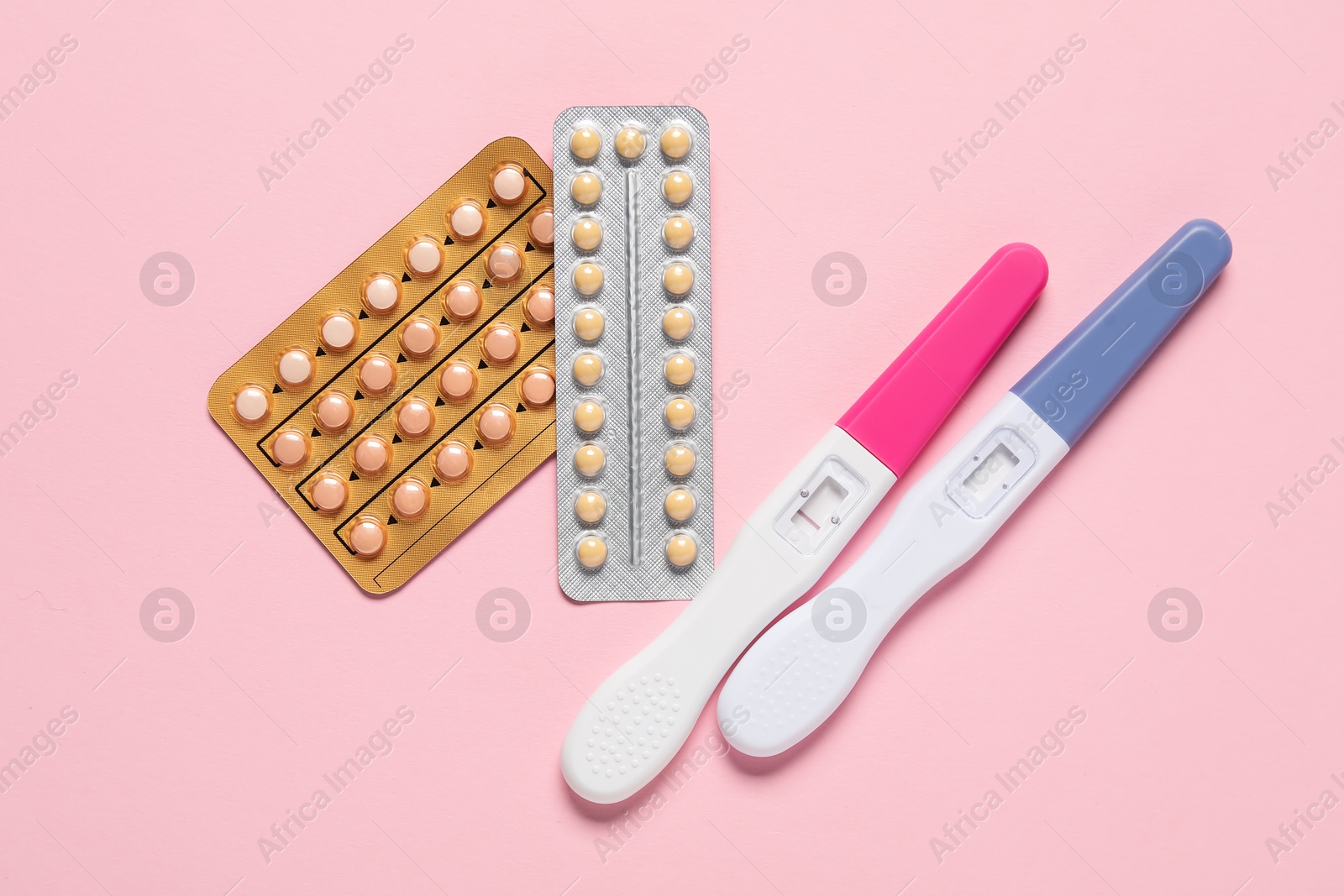 Photo of Blisters of oral contraceptive pills and pregnancy tests on pink background, flat lay