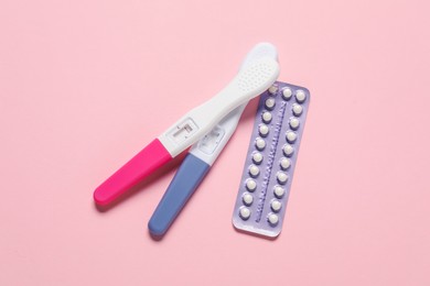 Blister of oral contraceptive pills and pregnancy tests on pink background, flat lay