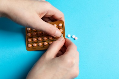 Photo of Woman taking contraceptive pill out from blister on light blue background, closeup