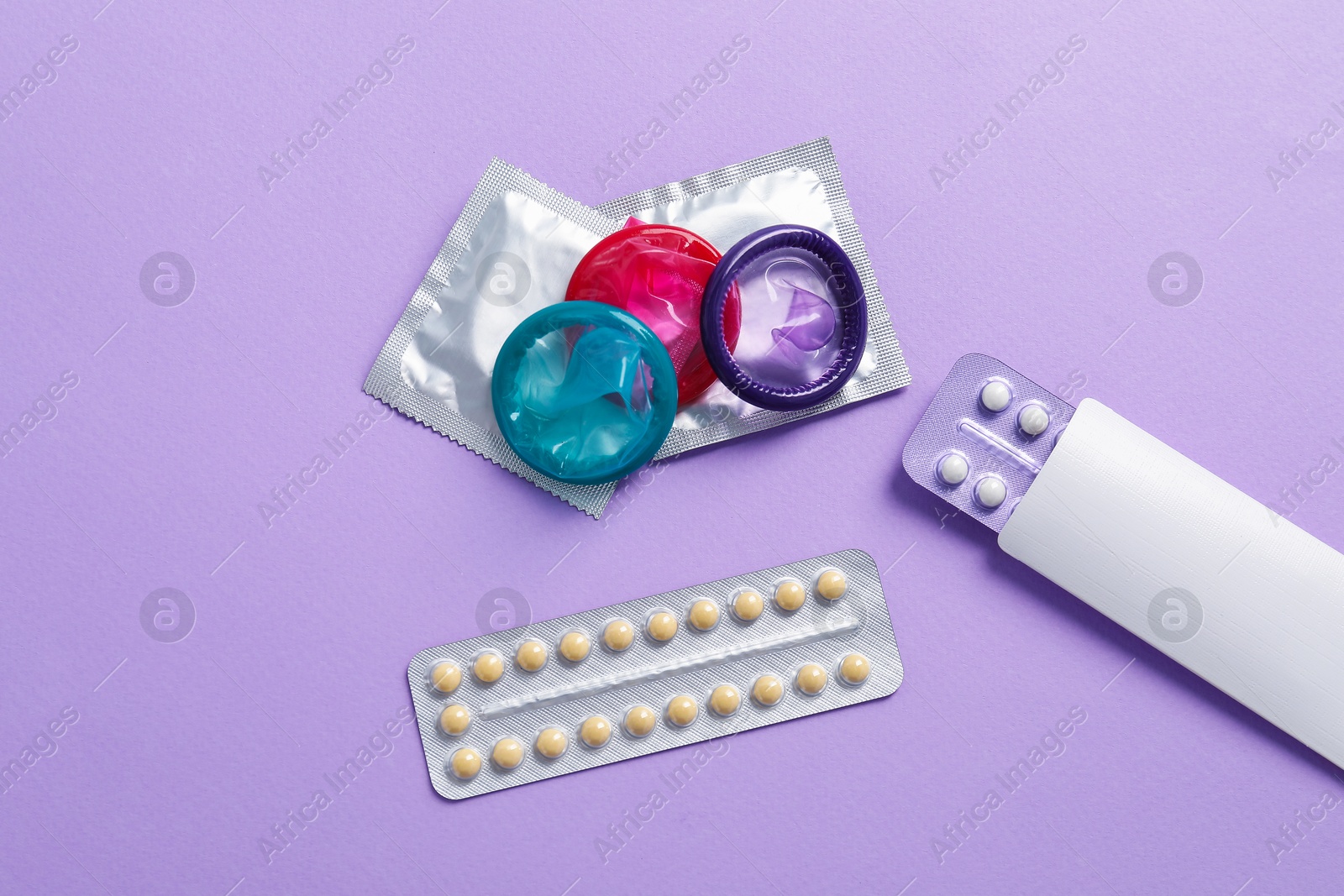 Photo of Blisters of contraceptive pills and condoms on lilac background, flat lay