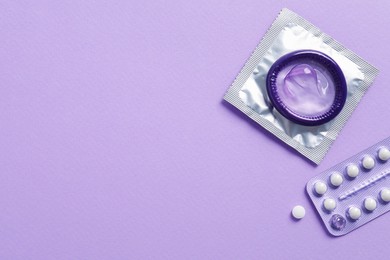 Photo of Blister of contraceptive pills and condoms on lilac background, flat lay. Space for text