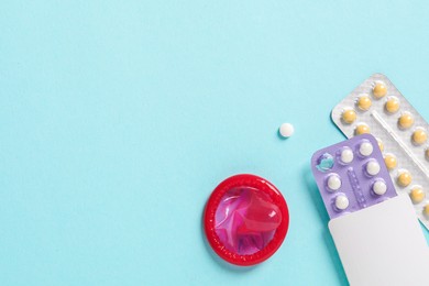 Photo of Blisters of contraceptive pills and condom on light blue background, flat lay. Space for text