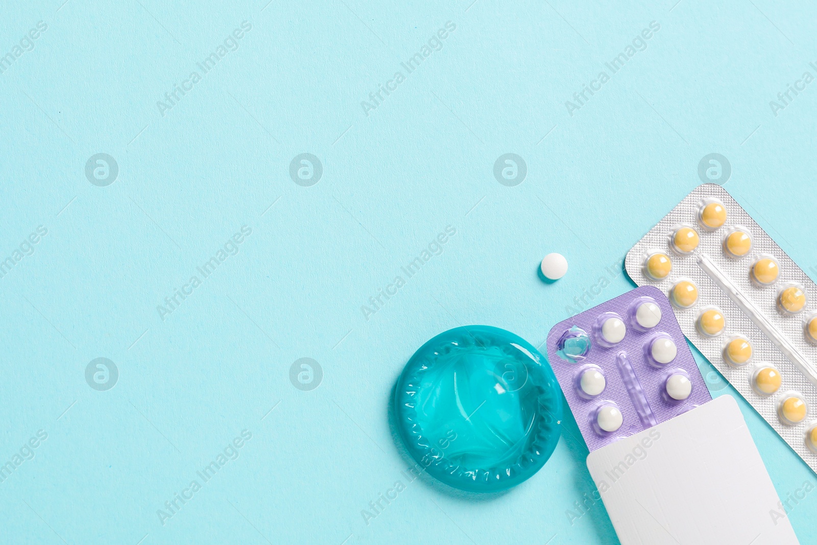 Photo of Blisters of contraceptive pills and condom on light blue background, flat lay. Space for text