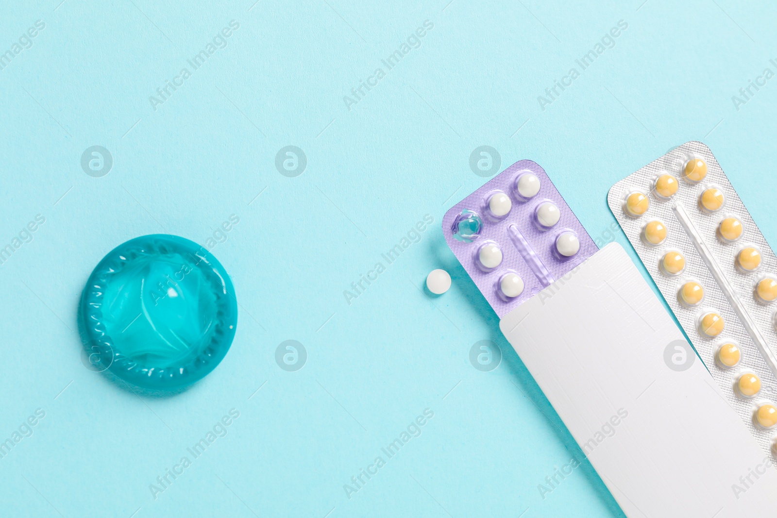 Photo of Blisters of contraceptive pills and condom on light blue background, flat lay