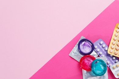 Photo of Blisters of contraceptive pills and condoms on pink background, flat lay. Space for text