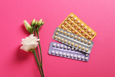 Blisters of contraceptive pills and eustoma flowers on pink background, flat lay