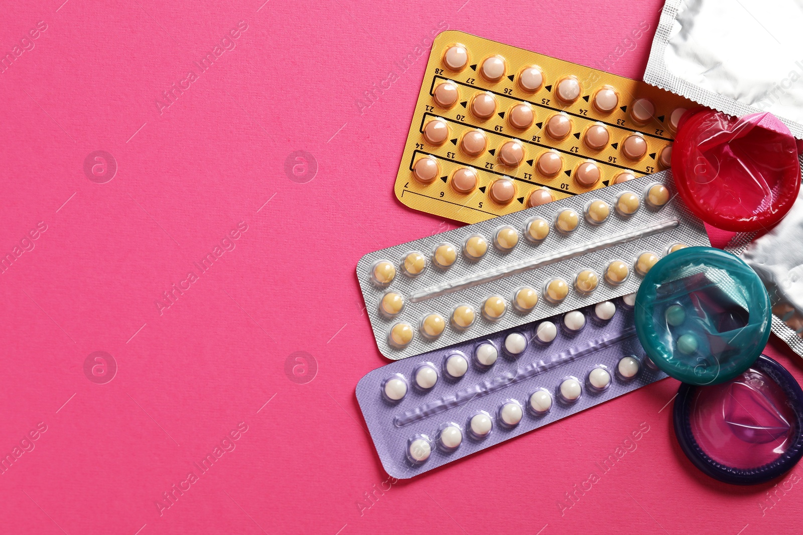 Photo of Blisters of contraceptive pills and condoms on pink background, flat lay. Space for text