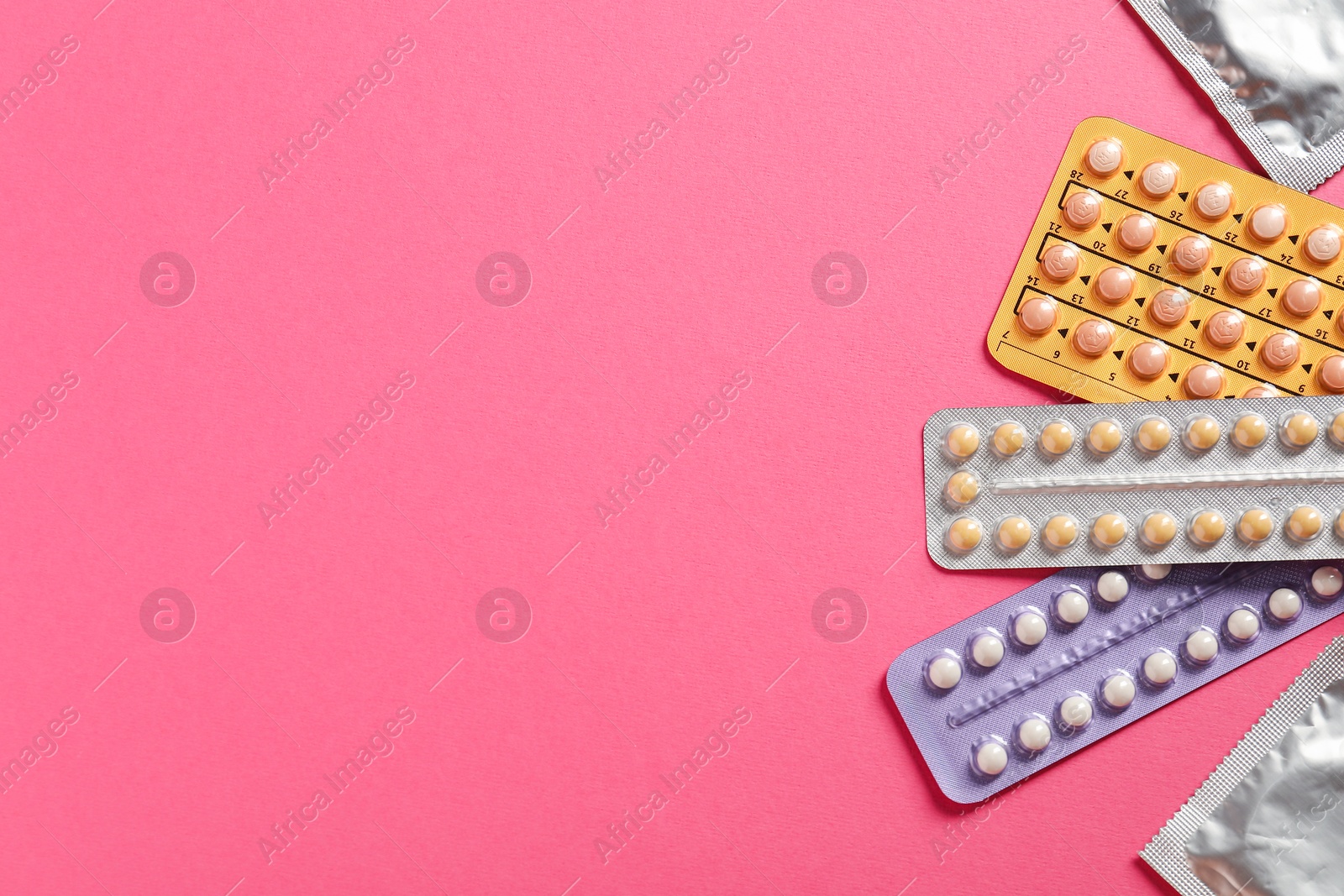 Photo of Blisters of contraceptive pills and condoms on pink background, flat lay. Space for text