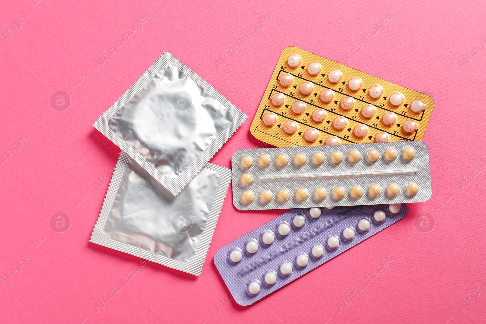 Photo of Blisters of contraceptive pills and condoms on pink background, flat lay