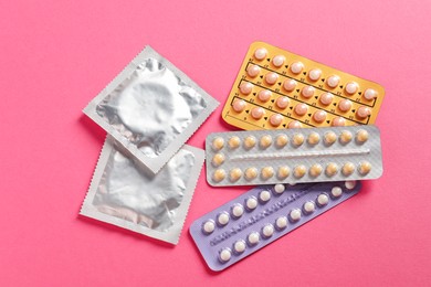 Photo of Blisters of contraceptive pills and condoms on pink background, flat lay