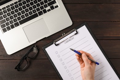 Photo of Woman filling Checklist at wooden table, top view