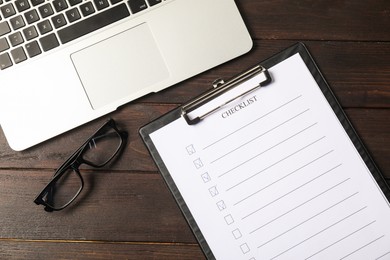 Photo of Checklist with checkboxes, glasses and laptop on wooden table, flat lay