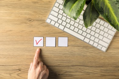 Photo of Woman pointing at checkbox with tick mark at wooden table, top view