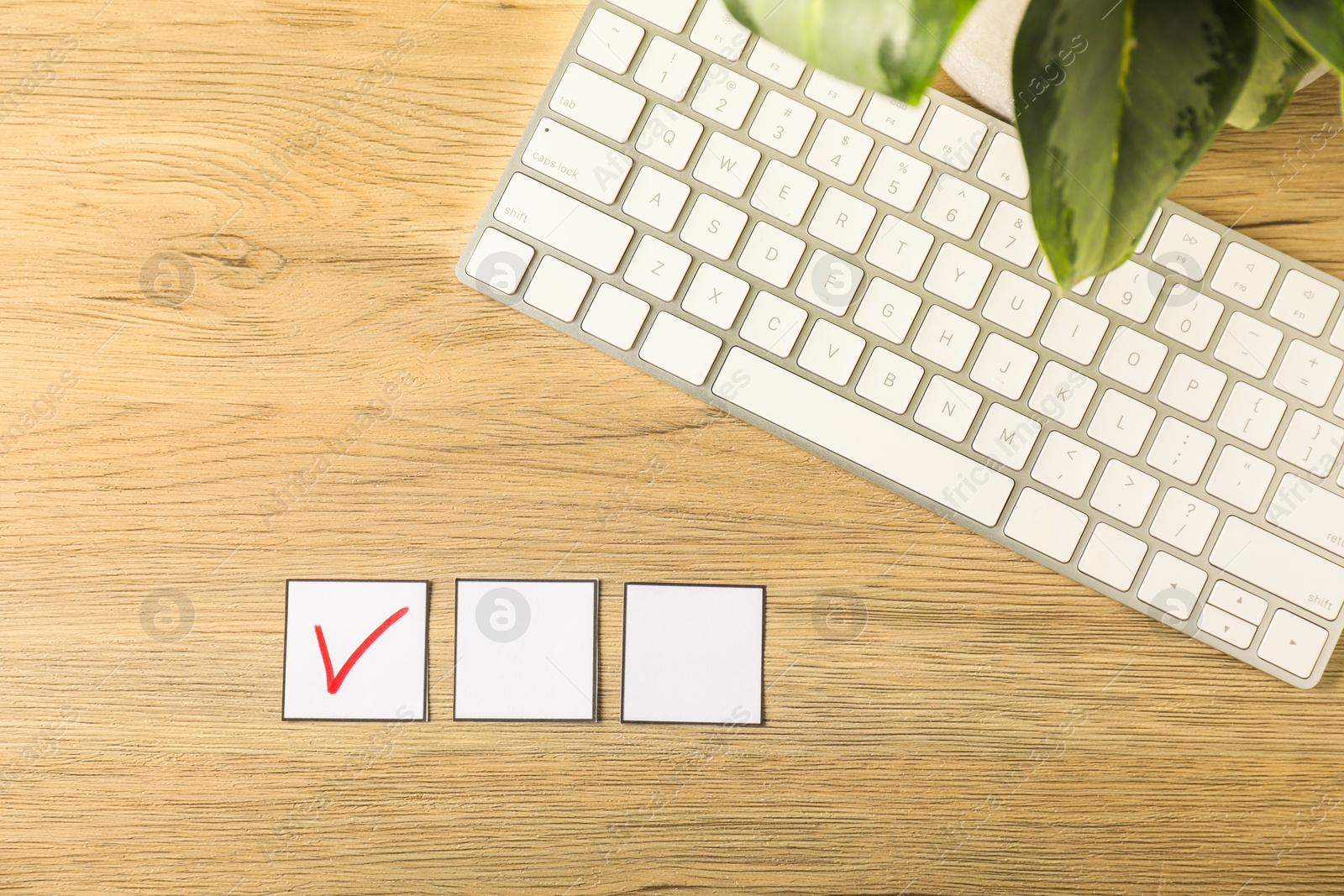 Photo of One checkbox with tick mark among others, computer keyboard and leaves on wooden table, flat lay