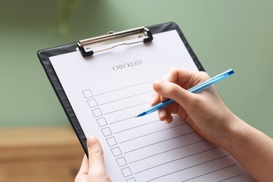 Photo of Woman filling Checklist with pen indoors, closeup