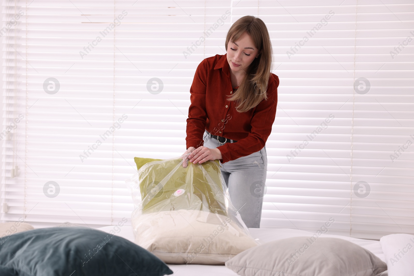 Photo of Woman packing pillow into vacuum bag at home