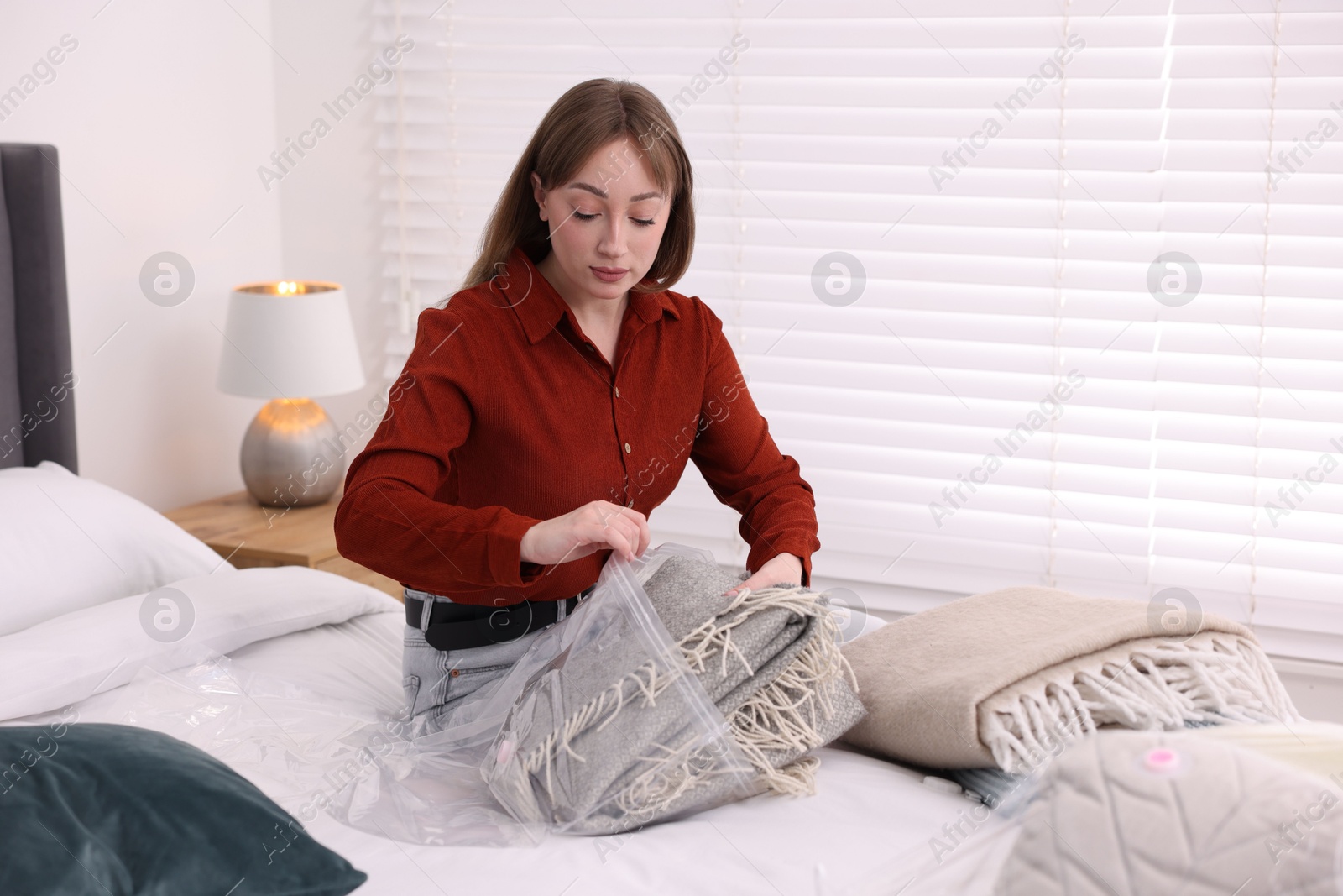 Photo of Woman packing blanket into vacuum bag on bed at home