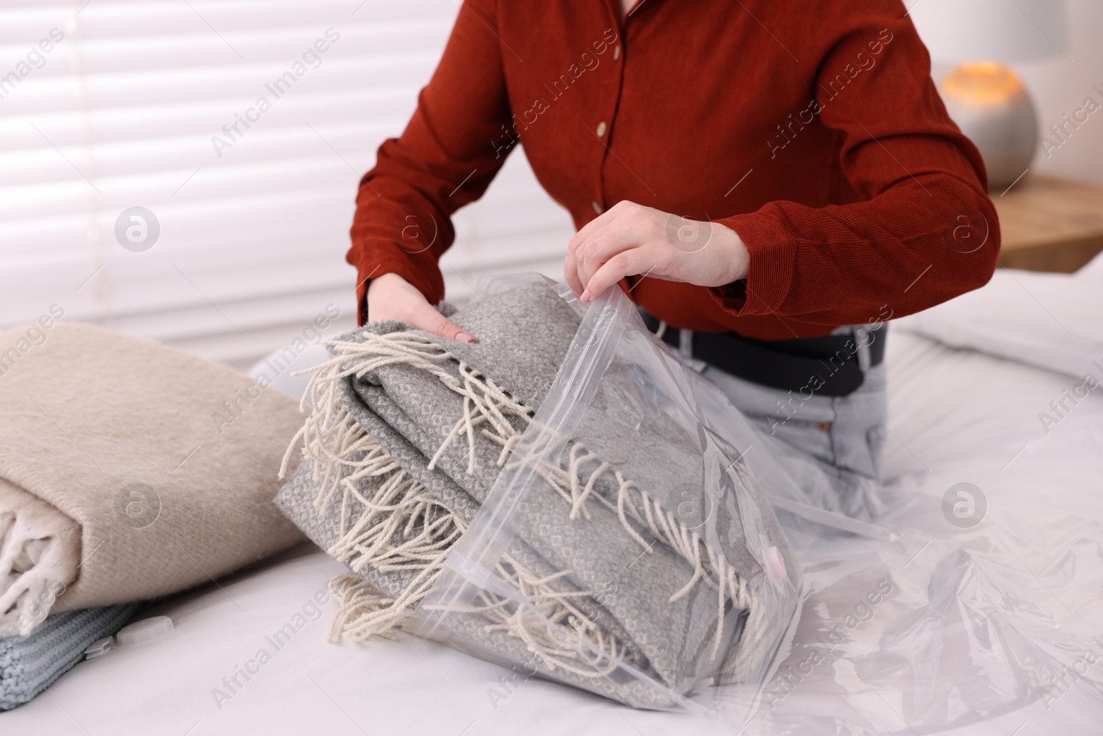 Photo of Woman packing blanket into vacuum bag on bed at home, closeup