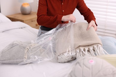 Photo of Woman packing blanket into vacuum bag on bed at home, closeup