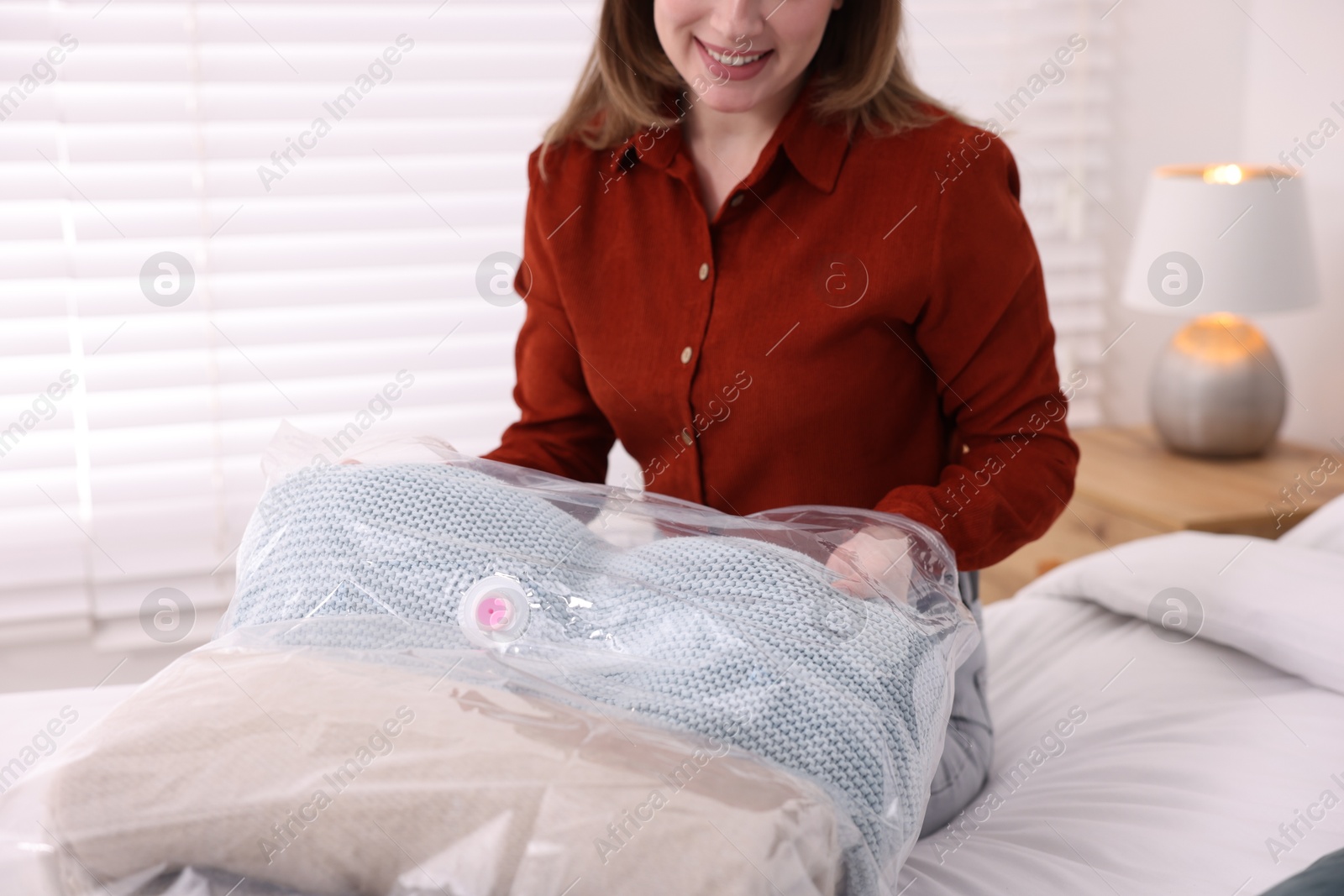 Photo of Woman packing blanket into vacuum bag on bed at home, closeup