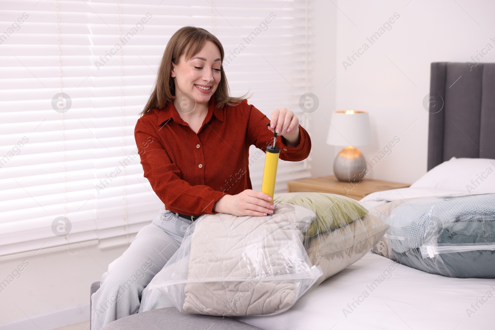 Photo of Woman sealing vacuum bag with pillows on bed at home