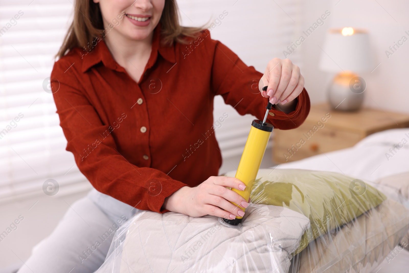 Photo of Woman sealing vacuum bag with pillows on bed at home, closeup