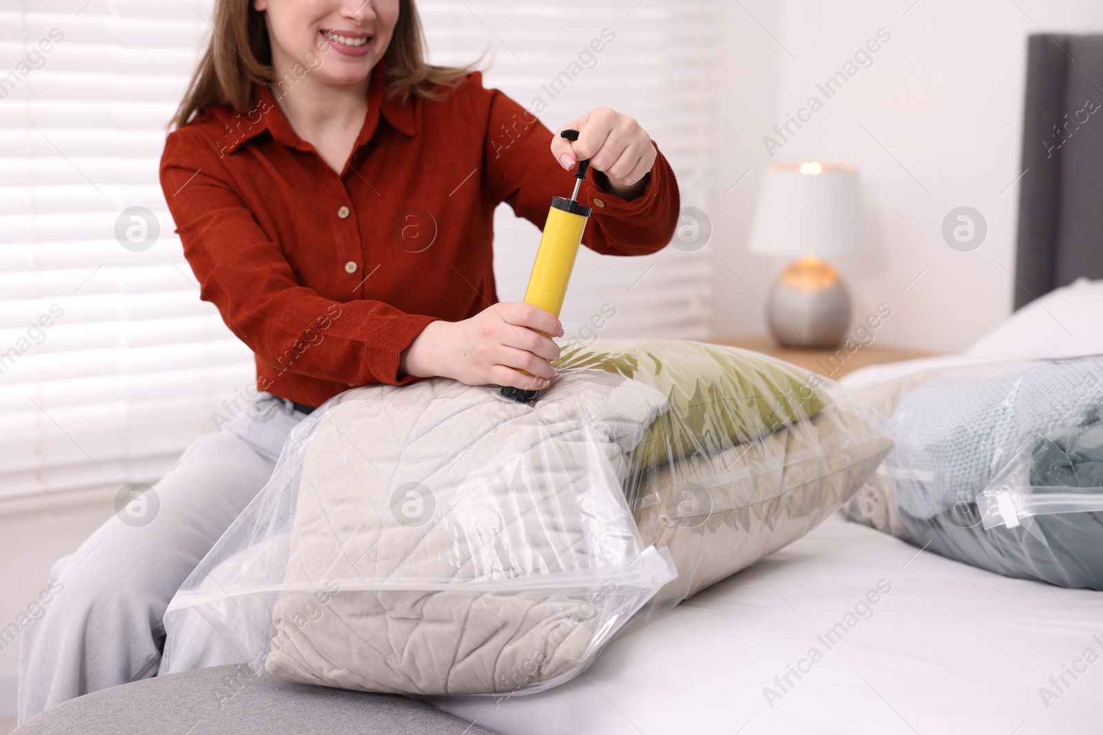 Photo of Woman sealing vacuum bag with pillows on bed at home, closeup