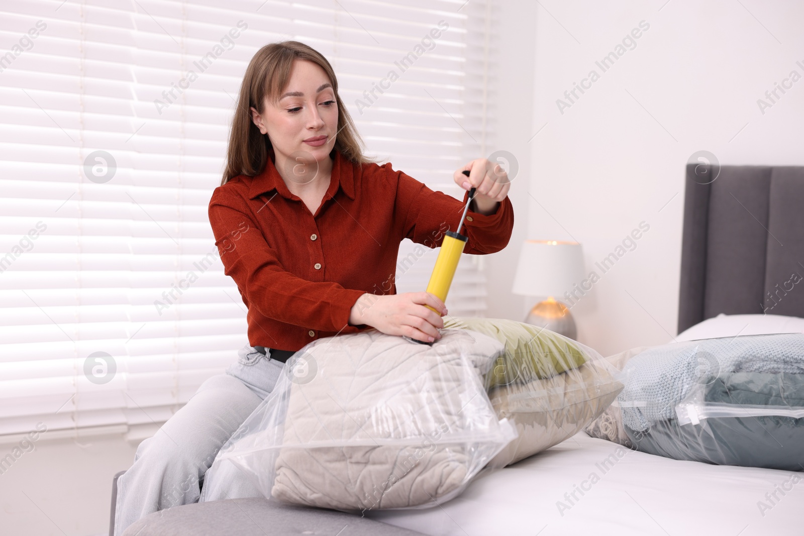 Photo of Woman sealing vacuum bag with pillows on bed at home